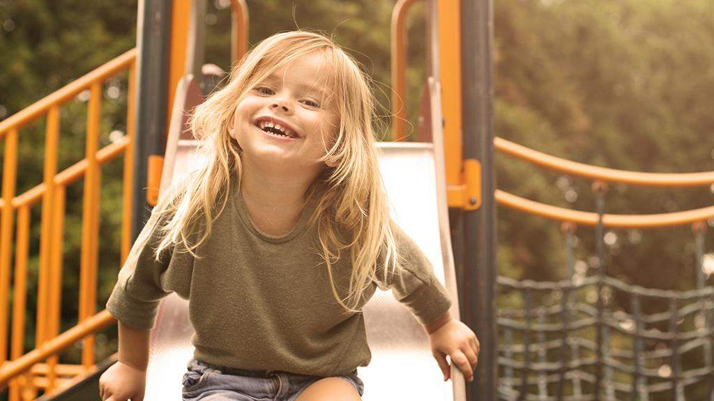 Fille souriante sur un toboggan dans une aire de jeux sans tabac